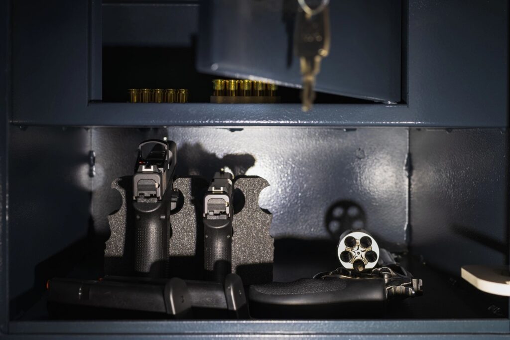 Pistols, a revolver and ammunition in a gun safe illuminated by a flashlight.