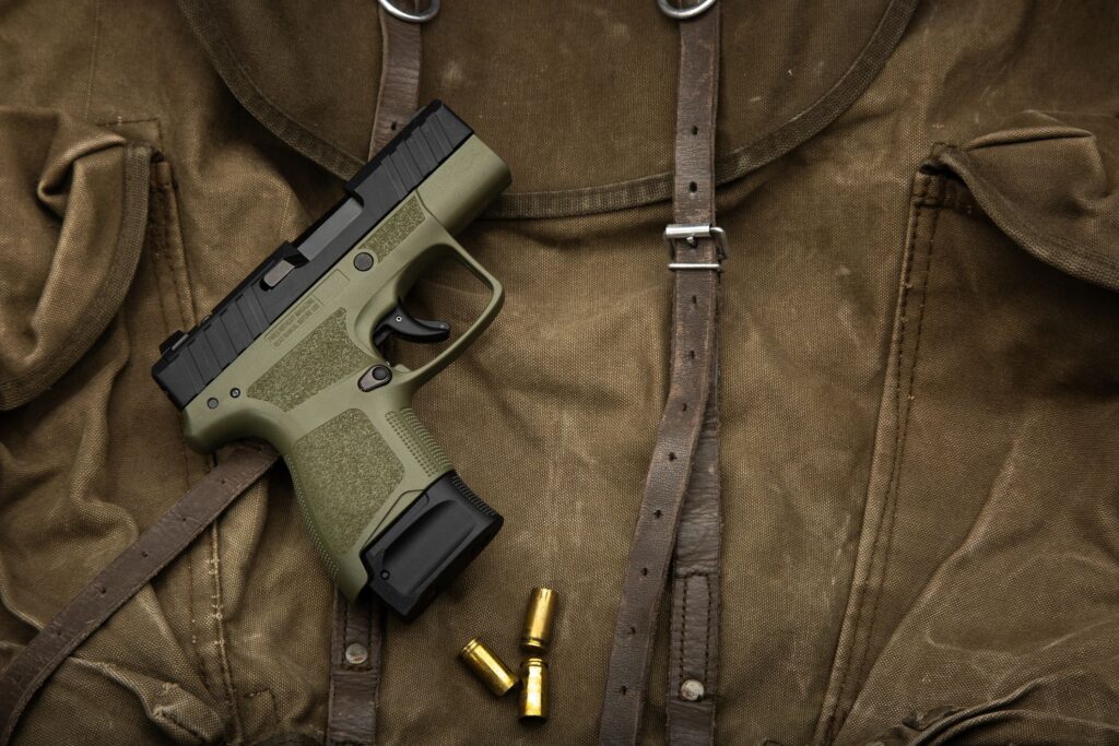 Olive green compact handgun with empty shell casings on a vintage canvas military bag.